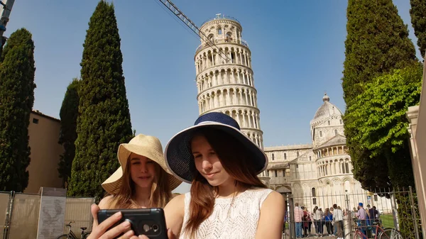 Duas jovens mulheres tiram uma selfie debaixo da torre inclinada de Pisa — Fotografia de Stock