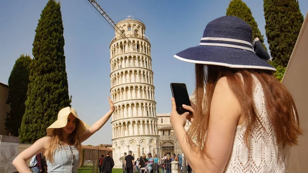 Zwei junge Frauen unter dem schiefen Turm von Pisa - eine von ihnen fotografiert andere. — Stockfoto