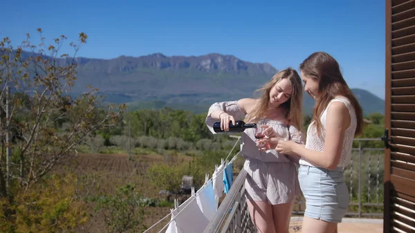 Дві молоді усміхнені жінки поливають вино на балконі — стокове фото
