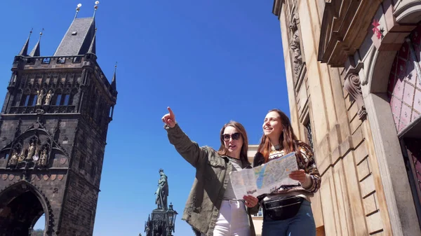 Dos mujeres jóvenes caminando debajo de la vieja torre y mira en el mapa —  Fotos de Stock