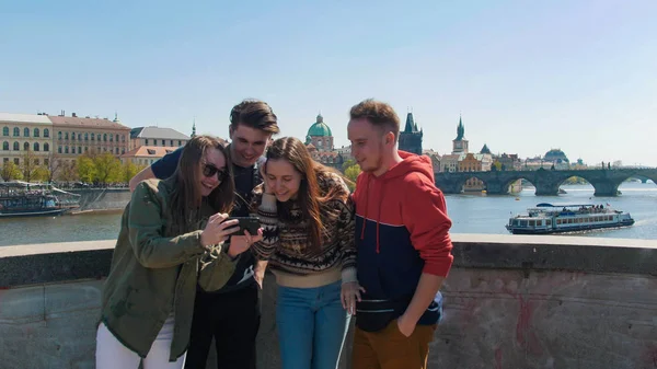 Companhia de amigos ficar na ponte e olhar foto no telefone. Checo, Praga — Fotografia de Stock