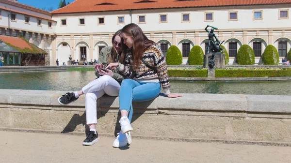 Dos mujeres jóvenes se sientan en la plaza y miran a su cámara. Checa, Praga —  Fotos de Stock