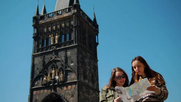 Dos mujeres jóvenes se paran en el fondo de la vieja torre y navegan por el mapa —  Fotos de Stock