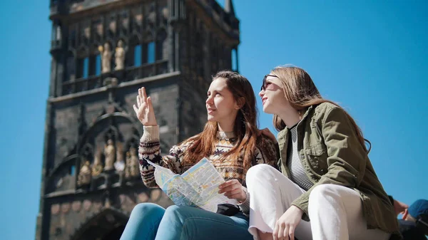 Dos mujeres jóvenes se sientan debajo de la vieja torre y se muestran el uno al otro barrio —  Fotos de Stock