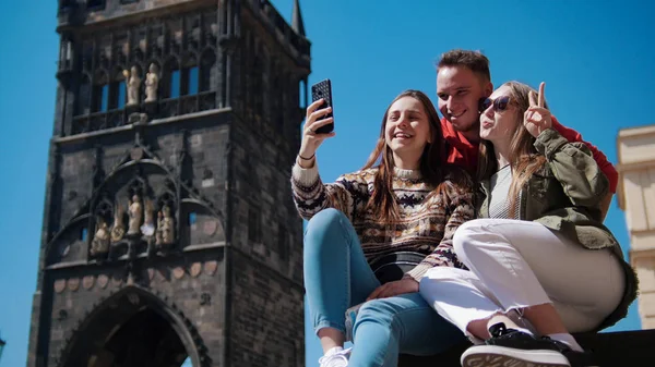 Tři mladí přátelé se usmívají a berou si pod starou věží Selži. Čeština, Praha — Stock fotografie