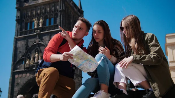 Three young friends navigate the map and looking right path under the old tower. Czech, Prague