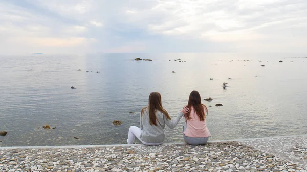Дві молоді жінки сидять на набережній і дивляться на узбережжя — стокове фото