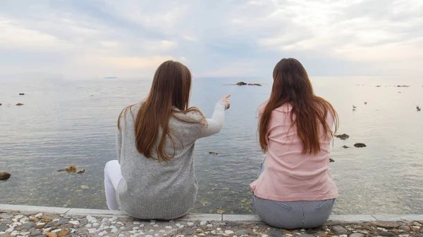 Deux jeunes femmes assises sur le front de mer et se montrent des oiseaux en mer — Photo