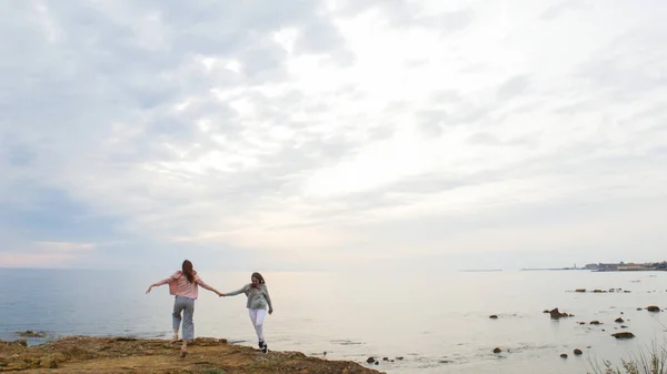 Deux jeunes femmes marchant sur le rivage rocheux près de la mer et les mains pendantes — Photo