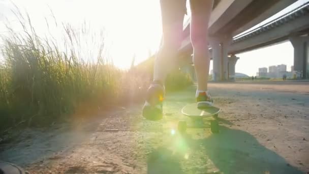 Mujer joven con buenas piernas monopatín debajo del puente urbano - la luz del sol brillante — Vídeo de stock