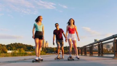 Genç arkadaşlar modern binaların bir arka plan üzerinde rıhtımda kaykay sürme - gün batımı