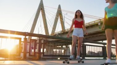 Genç kadınlar rıhtımda kaykaysürme - gün batımında büyük kentsel köprü
