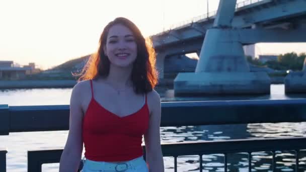 Jonge vrouw skateboarder staande op de waterkant bij zonsondergang — Stockvideo