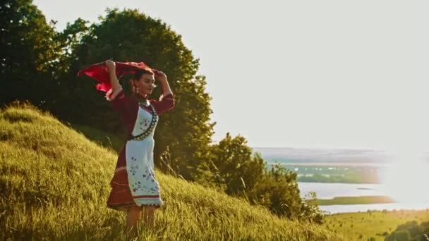 ロシアの民族衣装を着た若い女性が野原に立ち、景色を楽しんでいる - 彼女の頭の上にハンカチを置く — ストック動画