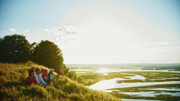 Les gens en vêtements russes traditionnels assis sur le terrain et parlant - beau paysage sur le coucher du soleil — Video