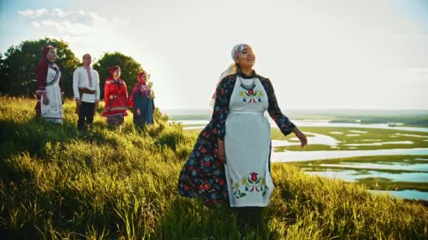 Jeunes en vêtements traditionnels russes debout sur le terrain et profitant de la vue sur le coucher du soleil — Video