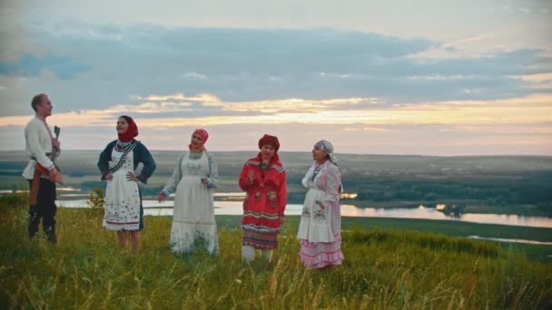Jonge mensen in Russische traditionele kleren staan op het veld op een achtergrond van de rivier en de eilanden — Stockvideo