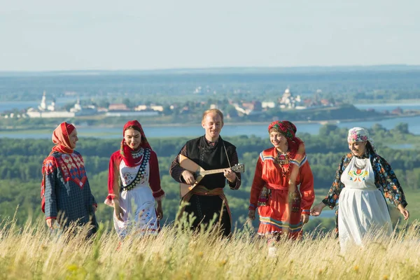 Улыбающиеся люди в традиционной русской одежде, идущие по полю - мужчина, держащий балалайку — стоковое фото
