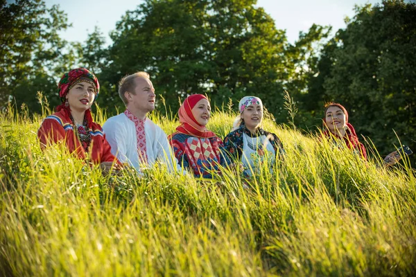 Улыбающиеся люди в традиционной русской одежде сидят на поле в высокой траве — стоковое фото