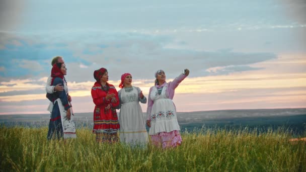 Люди в традиційному народному одязі стоять на полі і приймають селфі — стокове відео