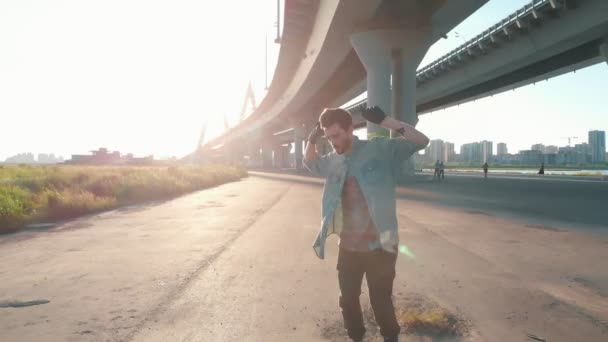 Молодой стильный мужчина танцует под мостом - идет прямо к камере — стоковое видео