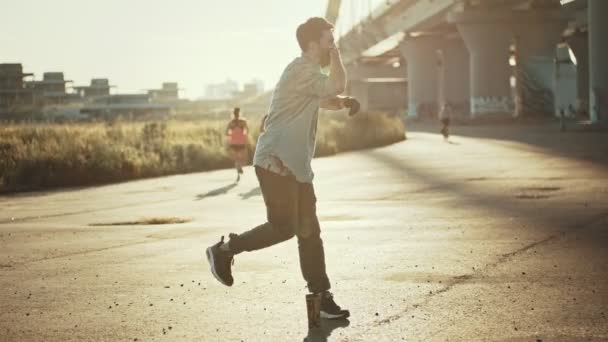 Mladý stylový muž, který si dělá volný styl do tancování nedaleko mostu-západ slunce — Stock video