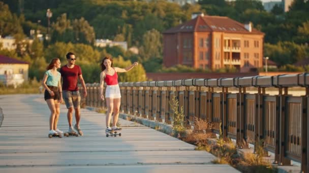 Os jovens amigos que montam skates em um cais em um contexto de edifícios modernos - pôr do sol — Vídeo de Stock