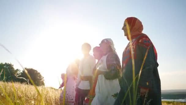 Женщины и мужчины в традиционной русской фольклорной одежде идут в ряд по полю и поют песню - яркий солнечный летний день — стоковое видео