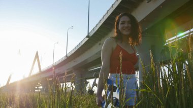 Yüksek çimenlerde duran ve kameraya poz veren kaykaylı genç gülümseyen kadın