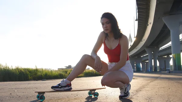 Giovane donna attraente seduta sullo skateboard sotto il ponte — Foto Stock