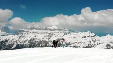 Dolomites'te karda büyük sırt çantalarıyla yukarı doğru yürüyen insanlar - bir kadın düşer ve adam ona yardım eder.