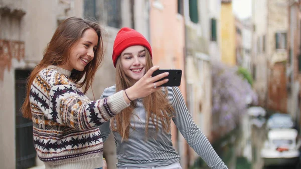 Дві молоді жінки в теплому одязі, що стоять на мосту і з селфі-Венеція, Італія — стокове фото