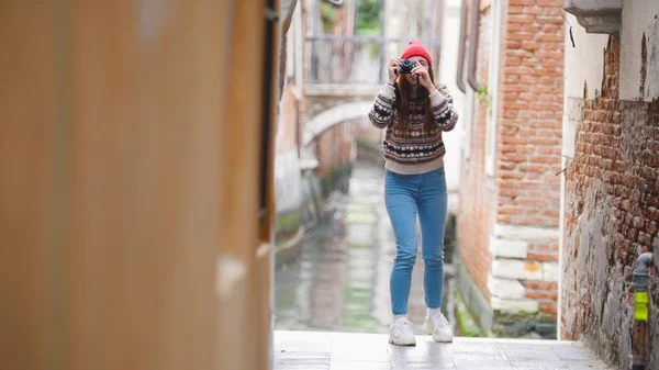 Una joven de pie cerca del canal de agua y tomando una foto en su cámara - Venecia, Italia —  Fotos de Stock