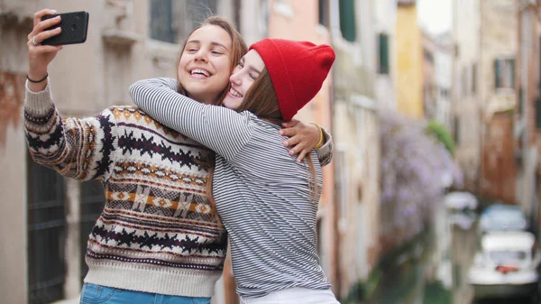 Δύο νεαρές γυναίκες με ζεστά ρούχα στέκονται στη γέφυρα και παίρνοντας μια selfie-αγκαλιάζοντας-Βενετία, Ιταλία — Φωτογραφία Αρχείου