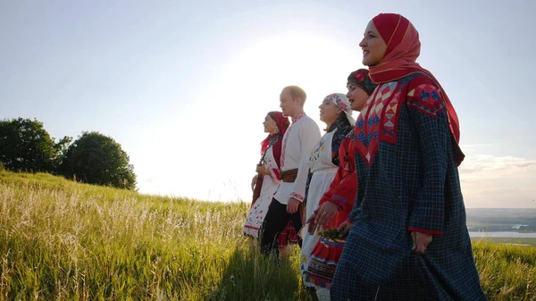 People in traditional russian clothes walking in a row on a meadow and singing a song