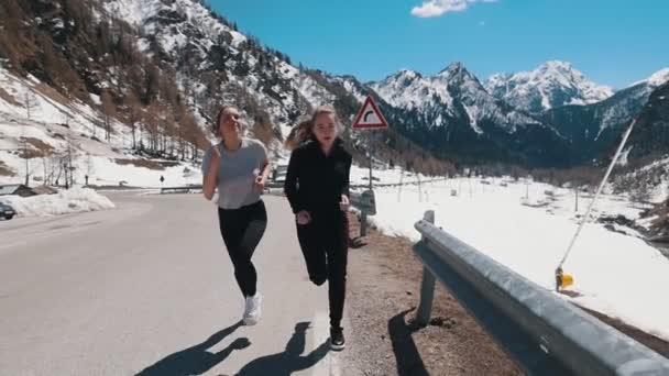 Két fiatal nő fut az úton a háttérben og a hegyek-Dolomitok, Olaszország — Stock videók