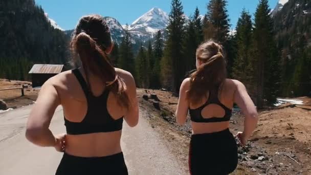 Dos jóvenes deportistas en sujetador deportivo corriendo en la carretera - Dolomitas, Italia — Vídeos de Stock