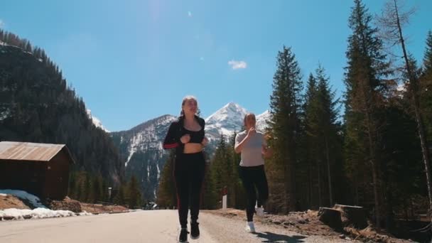 Duas jovens mulheres esportivas correndo na estrada cercadas por floresta - Dolomites, Itália — Vídeo de Stock