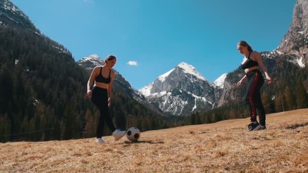 Dağların ve ormanın arka planında futbol topuyla oynayan iki genç kadın — Stok video