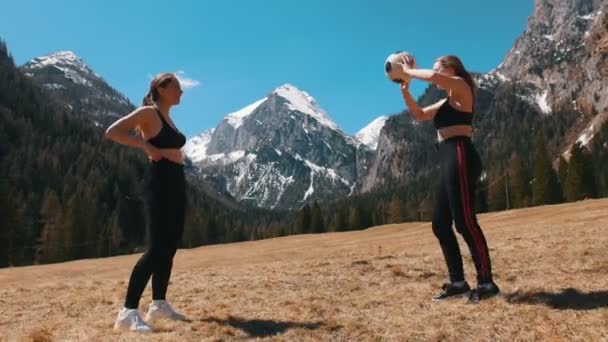 Two young women playing with a football ball on a background of the mountains and forest - Dolomites, Italy — Stock Video