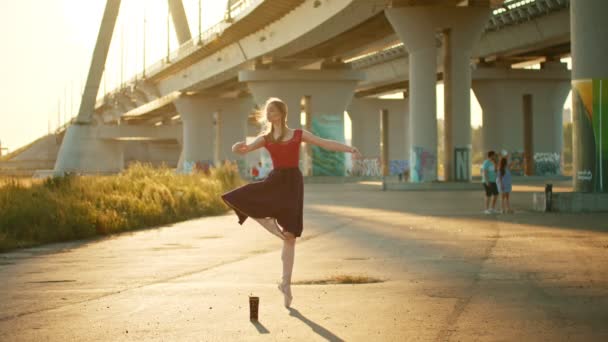 Молодая балерина танцует у моста на закате — стоковое видео