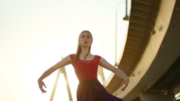 Mujer joven bailarina bailando cerca del puente en la puesta del sol - realizar un elemento y reír — Vídeo de stock