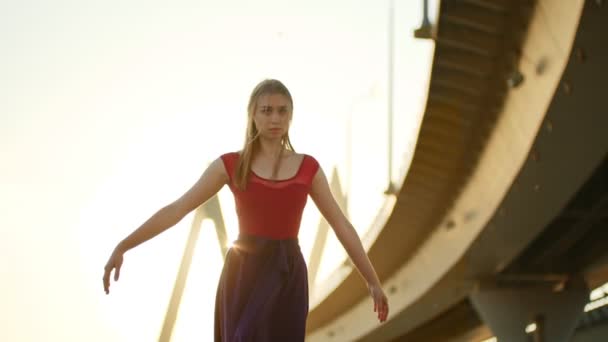 Mladá žena baletka tancuje nedaleko mostu na západ slunce a dělá prvek — Stock video