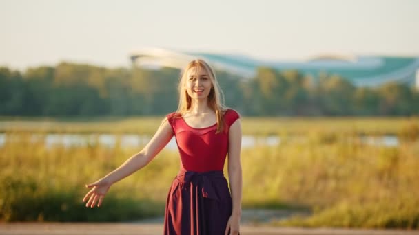 Una mujer rubia muy sonriente agitando la mano en la cámara - campo y lago — Vídeos de Stock