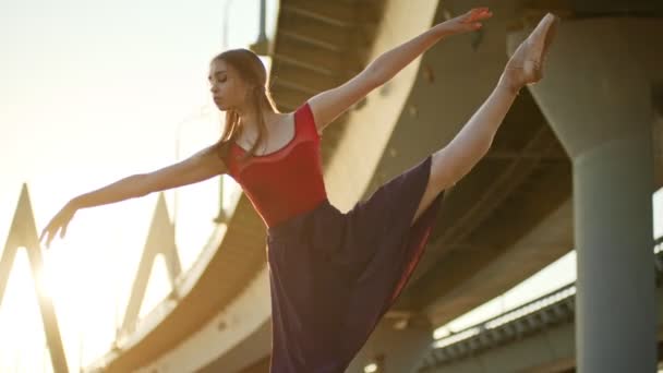 Bailarina de mujer joven en falda ligera bailando cerca del puente al atardecer - realizando un elemento — Vídeo de stock