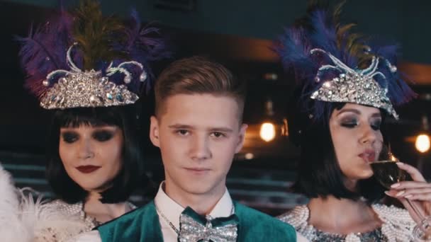 Stylish young man in tuxedo surrounded by luxurious smiling women throws up a stack of bills. — Stock Video