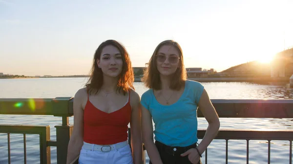 Giovani donne skateboarder in piedi sul lungomare sullo sfondo del fiume - tramonto — Foto Stock