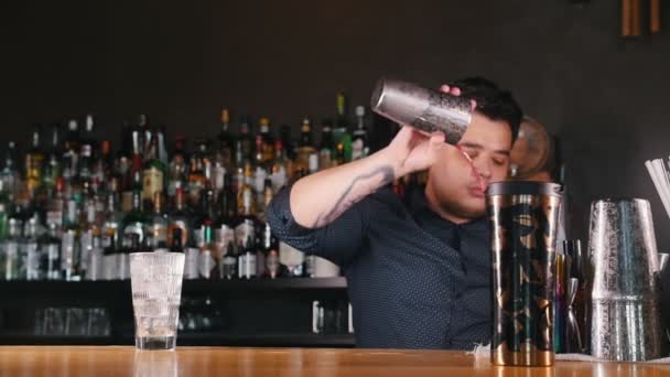 Jovem barman profissional derrama um copo de líquido em uma coqueteleira — Vídeo de Stock