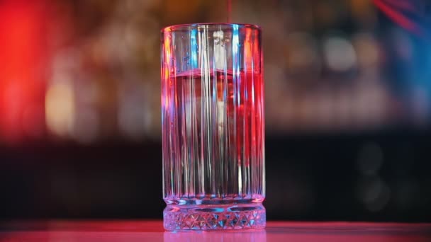 Bar Concept-en röd sirap hälls i ett glas med en klar vätska-neonrosa belysning — Stockvideo