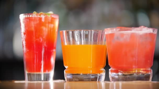 Barkonzept - drei Gläser mit Cocktails stehen auf dem Regal. Eis fällt von oben — Stockvideo